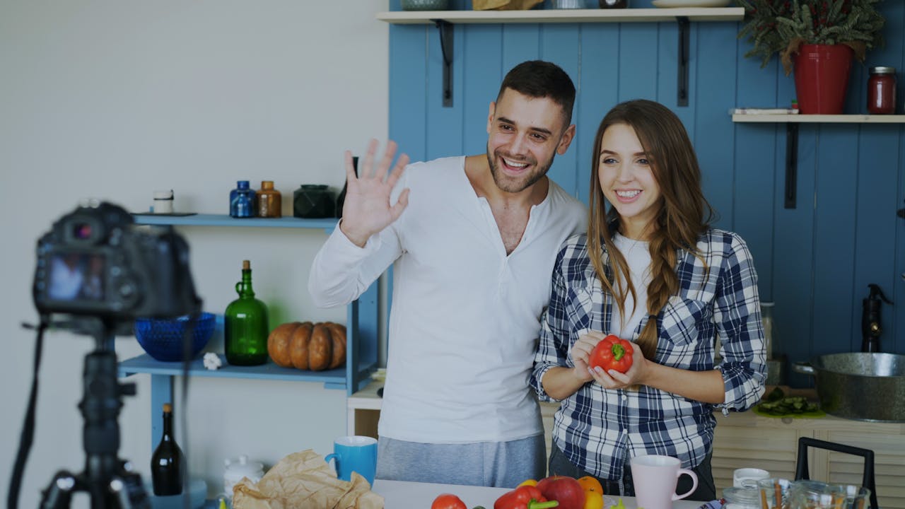 Smiling couple filming a cooking vlog in a modern kitchen setting, engaging viewers.