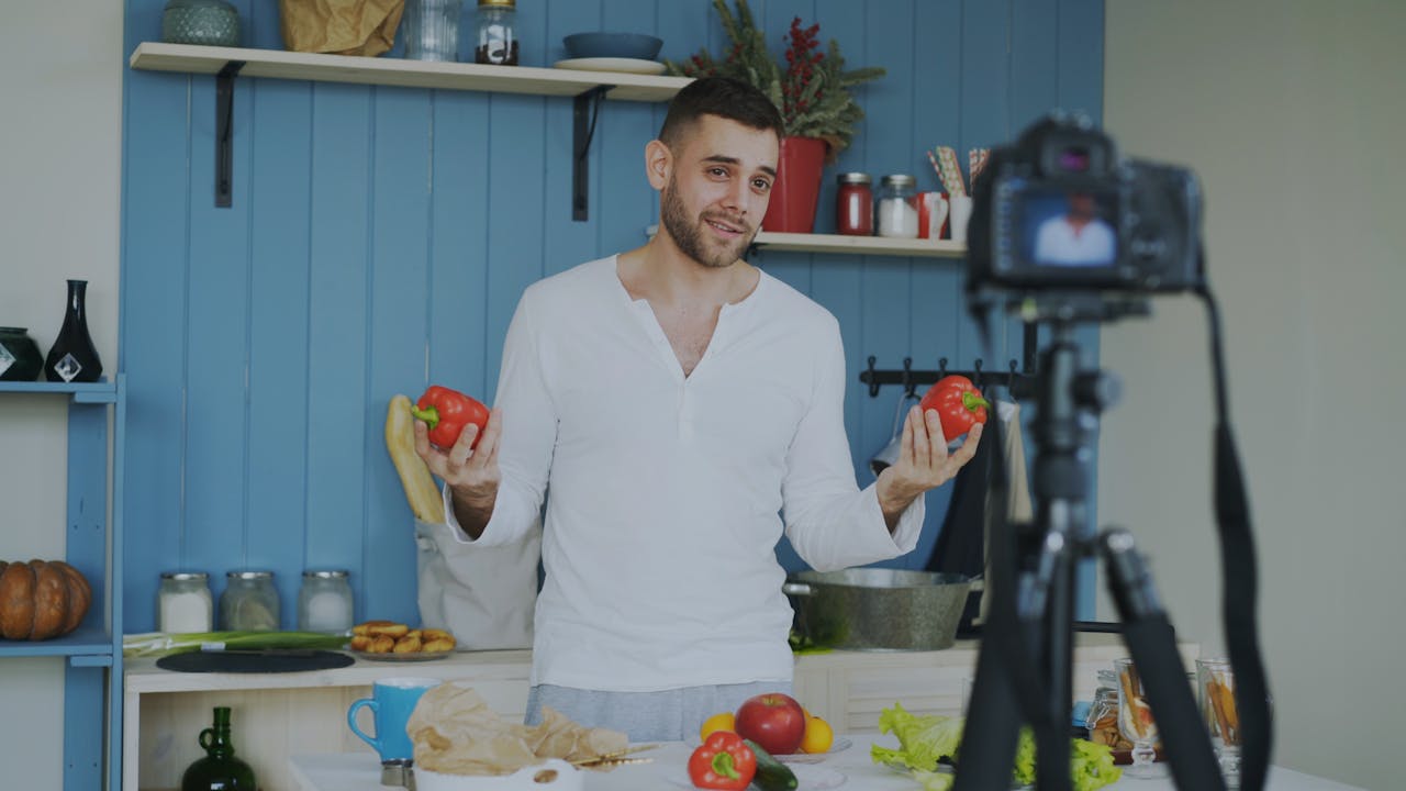 contact-img Man in kitchen filming cooking video with fresh vegetables. Lifestyle content creation.